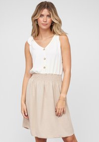 Haut sans manches blanc avec un décolleté en V et trois boutons, associé à une jupe beige mi-longue avec une taille élastiquée froncée.