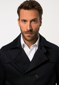 Abrigo azul marino de doble botonadura con cuello con muesca, detalles de botones y una textura suave, superpuesto sobre una camisa blanca.