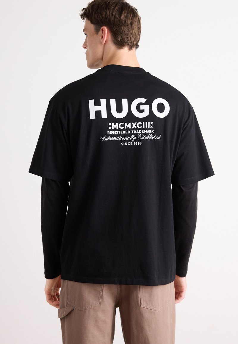 Svart bomull T-skjorte med hvit "HUGO" logo og tekst på baksiden, korte ermer og avslappet passform. Ensfarget tekstur, ingen mønstre.