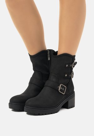 Botas negras de tobillo de ante con un tacón apilado, que cuentan con dos correas ajustables con hebilla y un zipper lateral para facilitar su uso.