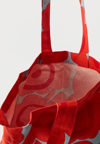 Czerwona torba materiałowa z długimi uchwytami, z dużymi wzorami kwiatowymi w odcieniach czerwieni i szarości zarówno na zewnątrz, jak i wewnątrz.