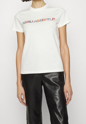 Camiseta blanca de algodón con un estampado gráfico multicolor de "KARL LAGERFELD" en el pecho, combinada con pantalones de cuero negros.