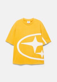 T-shirt jaune à manches courtes avec coupe oversize et grand graphique ovale blanc présentant deux formes d'étoiles à quatre branches sur le devant.