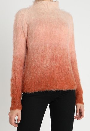 Pull doux et pelucheux à manches longues avec un dégradé du rose clair en haut à l'orange profond en bas, porté avec un pantalon noir.
