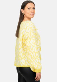 Geel gebreide trui met een gedurfde witte luipaardprint, ontspannen pasvorm, geribde manchetten en onderrand, en een lichte textuur.