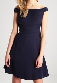 Marineblaue schulterfreie Kleid mit strukturiertem Stoff, tailliertem Oberteil und ausgestellt Rock für eine entspannte Silhouette. Keine sichtbaren Muster oder Beschläge.