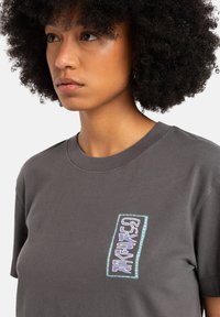 Gray cotton t-shirt featuring a colorful graphic patch with blue and purple text on the left side and a classic crew neck design.