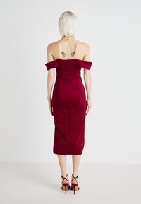 Robe midi bordeaux à épaules dénudées avec corsage ajusté, texture satin lisse, fentes sur les côtés et fermeture éclair à l'arrière. Sandales à talons hauts avec lanières.