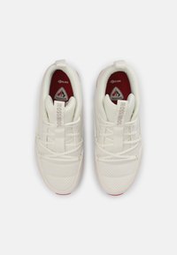 Scarpe sportive bianche con una tomaia texture, lacci elasticizzati, punta rinforzata e accenti rossi sulla suola. Logo del marchio visibile all'interno.