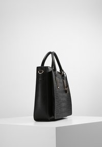 Sac à main en cuir noir avec un motif texturé de crocodile, ouverture supérieure, deux anses et des accents en métal doré. Vue latérale en présentation.