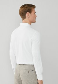 Witte langetermijn overhemd met een slim fit ontwerp en knoopmanchetten, gecombineerd met lichtgrijze gestructureerde broeken met een achterzak met een knoop.
