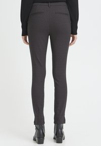 Black patterned trousers with a slim fit, featuring back pockets and a slight flare at the ankle, paired with black heeled boots.