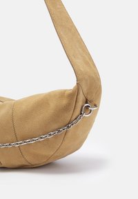 Suede handbag in a light tan color, featuring a rounded shape, thick shoulder strap, and a silver chain accent along the side.