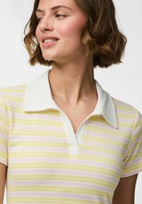 Camisa polo con cuello que presenta rayas horizontales en amarillo, rosa y blanco. La tela tiene una textura acanalada y el cuello es de color blanco sólido.