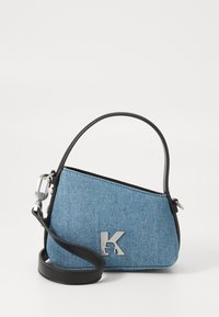 Bolsa de ganga com formato triangular, detalhes em pele preta, alça ajustável e acessórios em prata com um detalhe de logotipo.