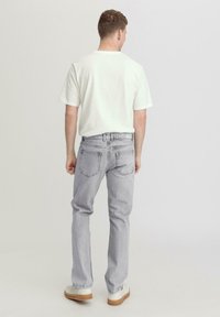 Light gray jeans with a straight leg fit, light denim fabric, five-pocket design, and stitched detailing. Complemented by a plain white T-shirt.