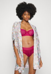 Robe leve, com padrão floral, feito de tecido suave, com mangas curtas. Por baixo, um soutien magenta sólido e um culote de cintura alta correspondente.