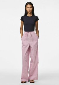 Zwarte aansluitende top met korte mouwen gecombineerd met losse, roze gestreepte wijde pijpen broek, met een elastische tailleband en zijzakken. Platte sandalen.