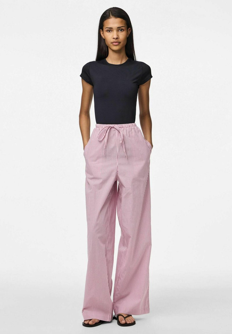 Zwarte aansluitende top met korte mouwen gecombineerd met losse, roze gestreepte wijde pijpen broek, met een elastische tailleband en zijzakken. Platte sandalen.