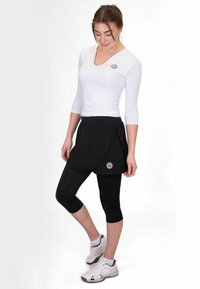 Top blanco ajustado con mangas de tres cuartos, combinado con una falda negra y leggings capri. Presenta el logo en la camiseta y en la falda.