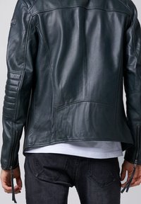 Giacca in pelle verde scuro con finitura texturizzata, caratterizzata da dettagli a coste sulle spalle, polsini con zip e una vestibilità su misura.