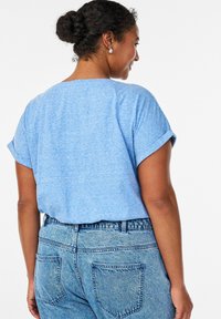 Blaues meliertes T-Shirt mit aufgekrempelten kurzen Ärmeln, kombiniert mit hoch taillierten hellblauen Jeans mit Gesäßtaschen.