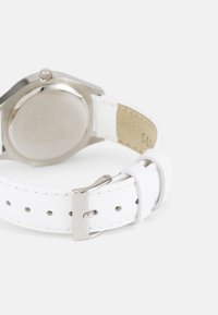 Weißes Lederarmband mit silberner Hardware, das über eine glatte Textur, eine verstellbare Schnalle und ein rundes metallisches Gehäuse auf der Rückseite verfügt.