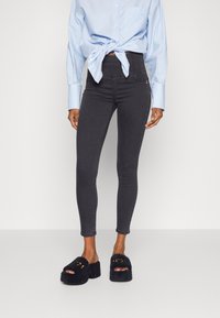 Vaqueros negros ajustados de cintura alta, combinados con sandalias negras peludas tipo slide con punta abierta y texto bordado en contraste.