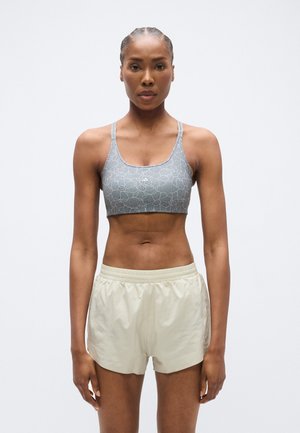 Top deportivo gris con estampado y tirantes finos, combinado con pantalones cortos deportivos beige claro de corte holgado y cinturilla elástica.