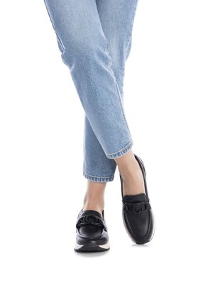 Zapatos de cuero negro tipo slip-on con punta redonda, que cuentan con una correa decorativa y una ligera plataforma, usados con jeans de corte recto de color azul claro.