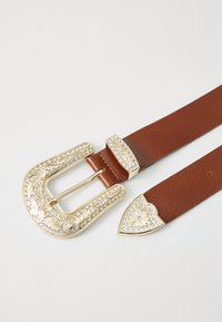 Ceinture en cuir marron avec une large boucle en or ornée de gravures florales et de strass transparents. L'extrémité possède un accent doré en forme de triangle.