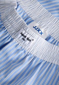 Vêtements à taille élastique rayés verticalement bleu et blanc avec deux étiquettes blanches portant les inscriptions "JJXX" et "Apparel Studio JJXX".