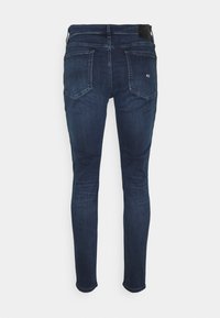 Mörkblå tajta jeans i denim, med två bakfickor, midjehöjd och en svart midjebandsetikett. Slät yta.