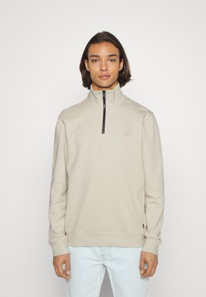 Beige, lange mouw sweatshirt met hoge kraag en kwart-rits. Heeft geribbelde boorden en zoom, met een logopatch op de borst. Gladde textuur.