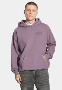 Fioletowa bawełniana bluza z kapturem z kieszenią kangurka, o luźnym kroju i nadrukiem na piersi. Posiada sznurek przy kapturze i ściągacze przy rękawach.