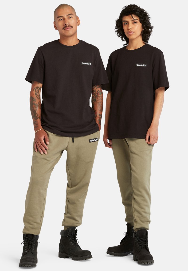 Svarte bomulls t-skjorter med Timberland-logo, kombinert med olivengrønne joggebukser med merkevare, og svarte snørestøvler med teksturerte såler.