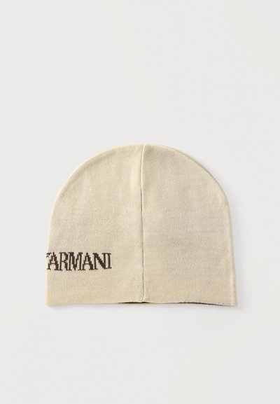 Bonnet tricoté beige avec une couture centrale et un texte brun foncé partiellement visible "ARMANI" sur le côté gauche.