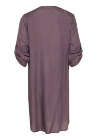 Chemise longue et ample de couleur mauve douce. Texture lisse, encolure ronde et manches repliées avec détail de bouton. Design simple, sans motifs.