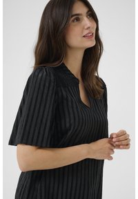 Blusa a righe nere con maniche corte, caratterizzata da un corpetto testurizzato e un collo a V. Il tessuto ha un aspetto morbido e leggermente stropicciato.