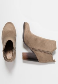 Beżowe zamszowe botki za kostkę o zwężającej się sylwetce, z bocznym zamkiem błyskawicznym i obcasem typu stacked z efektownym gradientem. Gładka faktura, minimalistyczny design.