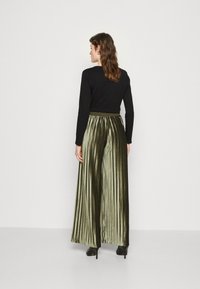 Maglia nera a maniche lunghe abbinata a pantaloni a vita alta verde oliva con pieghe in morbido velluto, caratterizzati da un design a gamba larga e tacchi a spillo neri.