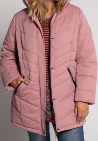Abrigo parka acolchado rosa con capucha, patrón de acolchado diagonal, cremallera negra y bolsillos laterales. Camiseta a rayas debajo.