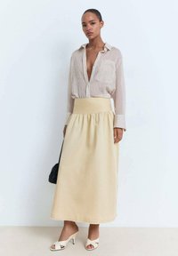 Camicia a righe, con bottoni e vestibilità morbida; abbinata a una gonna maxi beige a vita alta e sandali con tacco color crema.