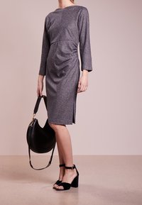 Robe grise texturée à manches longues, avec un détail froncé sur le côté, une fente latérale, associée à un sac à main noir et des sandales à talons carrés noires.