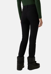 Black, fitted pants made of a stretchy material, featuring two back pockets. Mounted with black snow boots. Simple design with no visible accents.