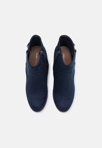 Botas de tobillo azul marino con un acabado de ante, con cremalleras laterales y punta redondeada, mostradas desde una vista superior.