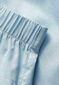 Tissu bleu clair avec ceinture élastique et couture cousue, probablement une partie d’un vêtement comme un pantalon ou un short.
