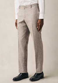Pantalones de lino gris claro con corte recto, que presentan bolsillos laterales y una sutil textura; combinados con mocasines negros.