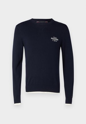 Mornarsko modra bombažna trenirka z dolgimi rokavi, ribanim ovratnikom in manšetami ter belim robom na dnu. Ponaša se z izvezenim logotipom "Tommy Hilfiger".