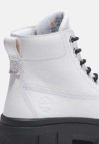 Botte en cuir blanc avec lacets noirs, talon surélevé et doublure en textile. Elle présente un logo gravé sur le côté et des coutures contrastées.